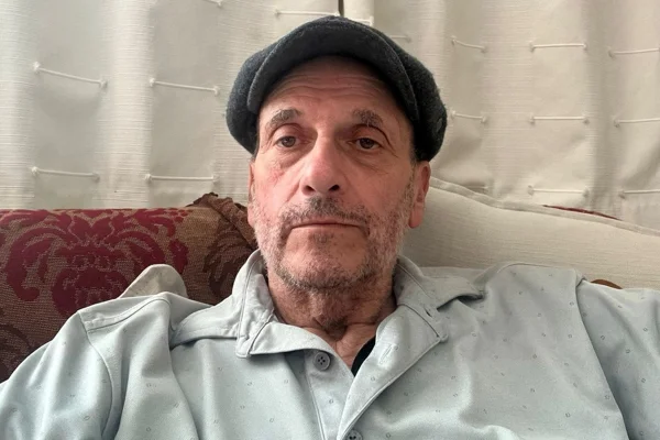 Foto colorida de homem com boina preta e blusa clara, olhando para foto. Metrópoles