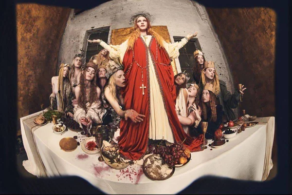 Mulher vestida de Jesus. Ela está em cima da mesa e rodeada por mulheres - Metrópoles