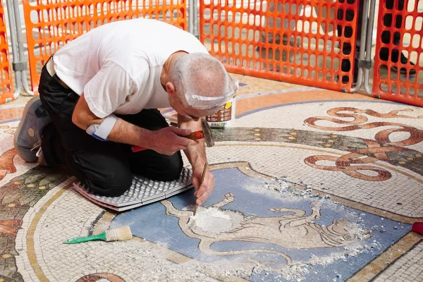 Um operário restaura os testículos do mosaico do touro no centro da Galleria Vittorio Emanuele II na Itália