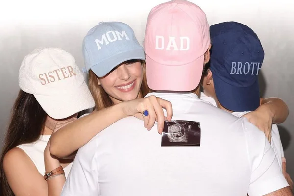 Foto colorida de Carol Celico mostrando uma foto da ultra da gravidez e abraçada com os filhos e marido - Metrópoles