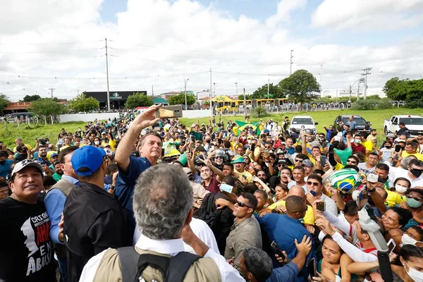 Presidente Bolsonaro durante partida da cidade de Caicó (RN) com o ex-senador Magno Malta. Ele está cercado por uma multidão verde e amarela, a maioria absoluta sem máscara, onde tira uma selfie - Metrópoles