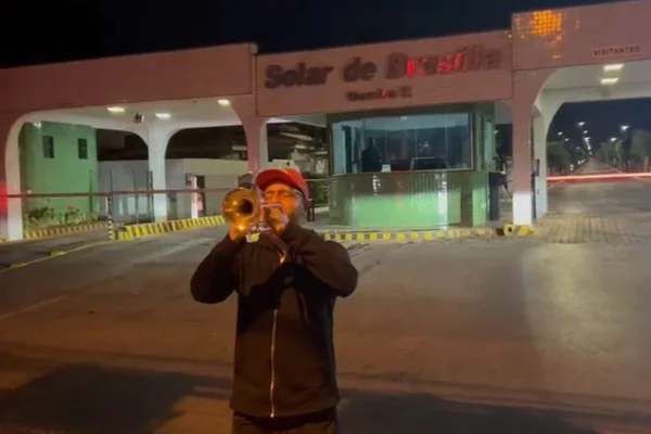 Imagem colorida de trompetista em frente ao condominio de Bolsonaro - Metrópoles