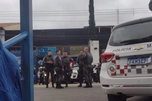Imagens coloridas mostram PMs reunidos na rua, uma viatura da Polícia Militar no canto direito, parte traseira à mostra, durante protesto de alunos