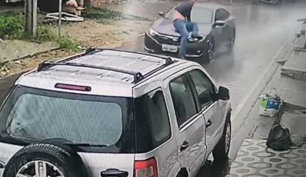 Homem agarrado a capô de carro
