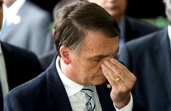 O presidente Jair Bolsonaro exibe semblante triste em evento, cercado por pessoas, com a mão no rosto e olho fechado - Metrópoles