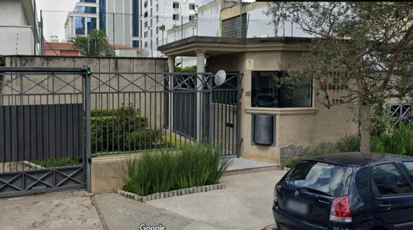 Portão cinza escuro de condomínio residencial, com guarita pintada de amarelo - Metrópoles