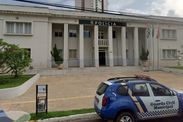 Imagem colorida de fachada de delegacia com um carro da polícia na frente. Metrópoles