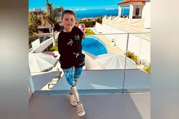 Harmonie Rose, menina de oito anos, posa em varanda com vista para piscina e jardim. Ela usa joelhos robóticos e não possui os braços - Metrópoles