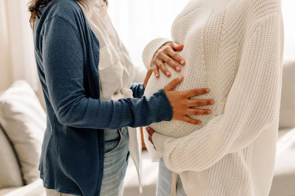 Foto colorida de uma mulher grávida e uma pessoa com a mão na barriga - Metrópoles