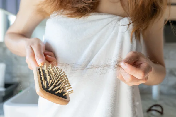 Foto de mulher de toalha com escova de cabelo em uma mão e mecha de cabelo na outra - Metrópoles