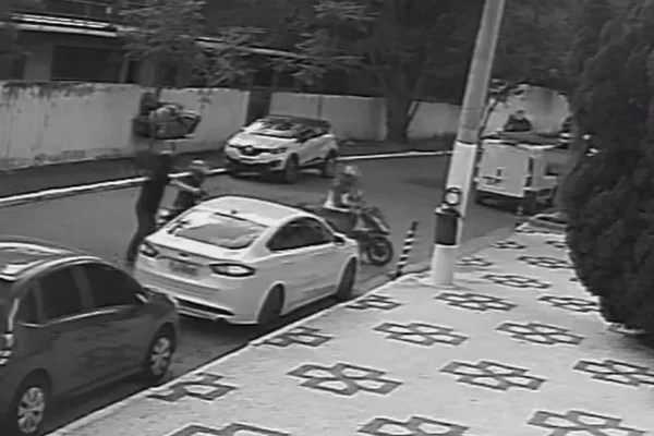 imagem em preto e branco mostra registro de câmera de segurança. cena mostra assaltante apontando arma para motorista de carro