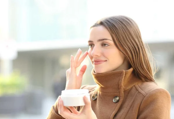 mulher no outono usando creme no rosto para cuidados - Metrópoles