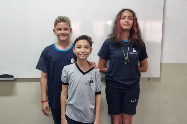 Três crianças em frente a um quadro de giz numa escola