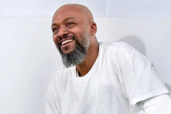 Na imagem colorida, homem de barba sorri e olha para cima. Ele usa blusa branca - Metrópoles