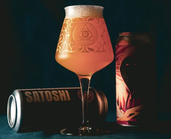 Na foto vemos duas latas de cerveja, uma em pé e outra deitada e uma taça cheia de cerveja