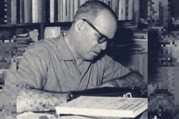 Imagem em preto e branco de Guimarães Rosa lendo um livro com biblioteca ao fundo - Metrópoles
