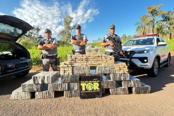 Imagem colorida mostra agentes da PM Rodoviária atrás de pacotes que somam mais de 500 kg de maconha apreendidos em carro em rodovia no interior de São Paulo - Metrópoles