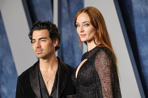 Foto colorida do cantor Joe Jonas e da esposa, a atriz Sophie Turner, posando em um fundo branco e azul - Metrópoles