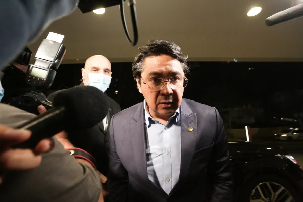 Imagem colorida mostra Alexandre Luiz Giordano andando sob microfones - Metrópoles