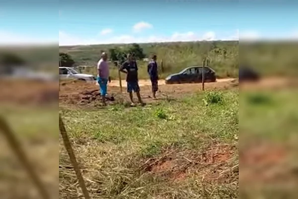 Homens em terreno de grama e carros na pista de barro atrás
