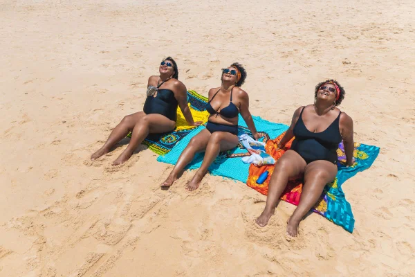 Foto colorida três mulheres na praia pegando sol no verão