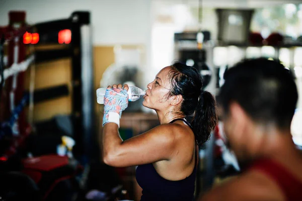 Foto colorida de uma mulher suada bebendo água durante o exercício físico - Metrópoles