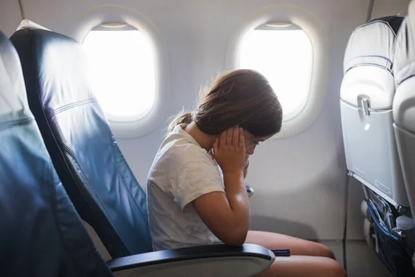 Menina com dor de ouvido no avião coloca mãos nas orelhas - Metrópoles
