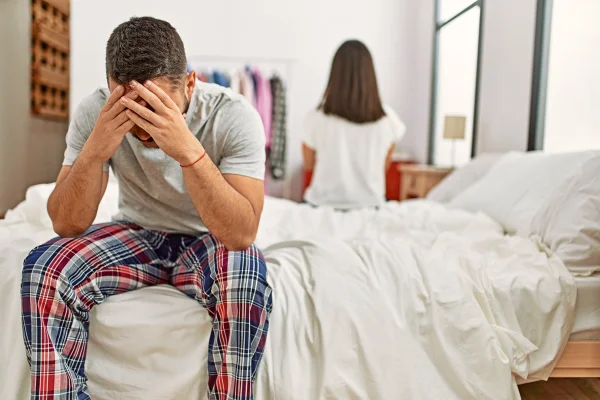 Foto colorida de casal separado na cama e home com expressão de frustração