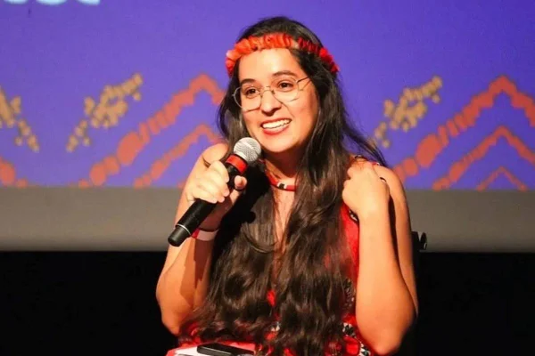 Imagem colorida de mulher indígena falando em microfone, com cabelo preto e solto - Metrópoles