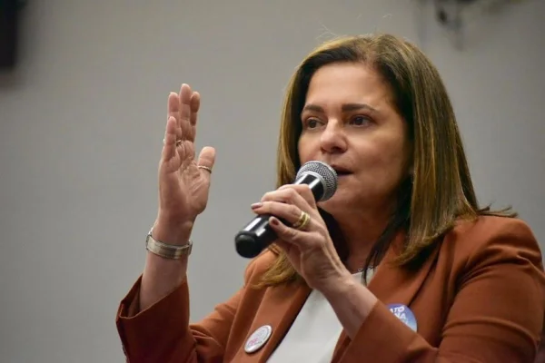 Mulher branca com cabelos lisos castanhos claros, na altura dos ombros. Ela veste um blazer marrom e camiseta preta e segura um microfone com uma das mãos - Metrópoles