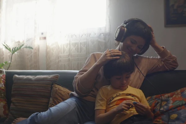 foto colorida de mulher sentada em sofa ouvindo musica com menino -metrópoles
