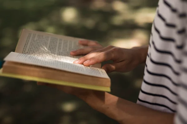 Imagem colorida, pessoa lendo um livro na natureza- Metrópoles