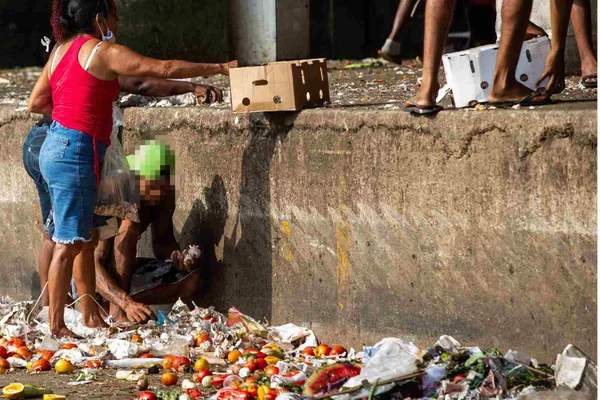 Imagem colorida de comida jogada no chão e pessoas catando - Metrópoles