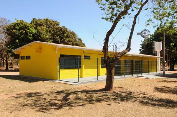 Casa amarela em chão marrom com árvores ao redor