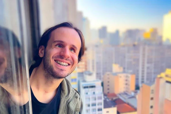 Foto colorida do influenciador Fernando Campos com a cabeça pra fora da janela - Metrópoles