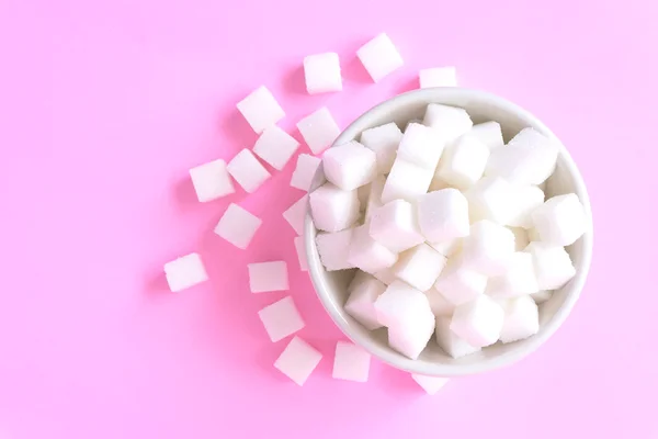Foto colorida de adoçante dentro de um pote branco e em um fundo cor-de-rosa - Metrópoles