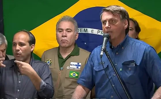 Bolsonaro discursa em Pernambuco após sobrevoar regiões afetadas pela chuva em Recife. Ele está ao lado dos ministros Queiroga e Augusto Heleno e do presidente da Caixa, Pedro Correia, bem como se tradutor. Ao fundo a bandeira do Brasil - Metrópoles