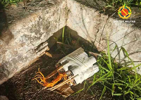 Imagem colorida de foguetes já desativados, enrolados em fitas brancas, jogados sobre uma pequena mata próxima a um meio-fio