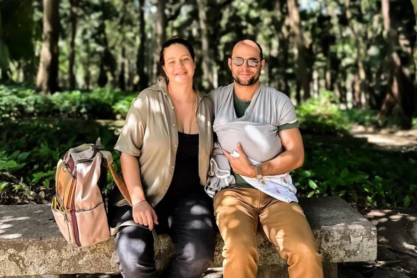 Imagem colorida de Leandra Leal, Guilherme Burgos e Damião em área verde, com carrinho de bebê e a criança no colo - Metrópoles