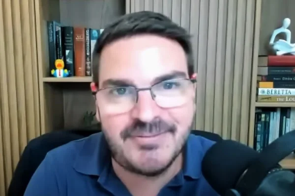 Imagem mostra o comunicador rodrigo constantino, de camisa azul, em frente a uma estante - Metrópoles
