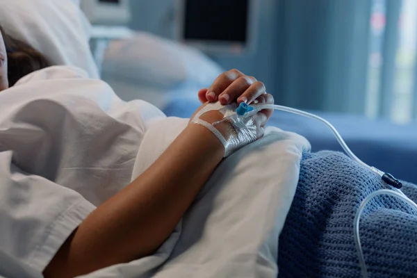Gotejamento, paciente e mão no hospital, assistência médica e intravenosa, vitaminas e medicamentos, sangue e tratamento. Cama, doente e pessoa na clínica, assistência médica e reabilitação, solução salina e cura na UTI. Metrópoles