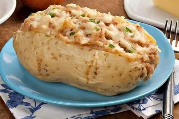 Batata recheada sob prato azul claro e mesa com talheres e guardanapo - Metrópoles