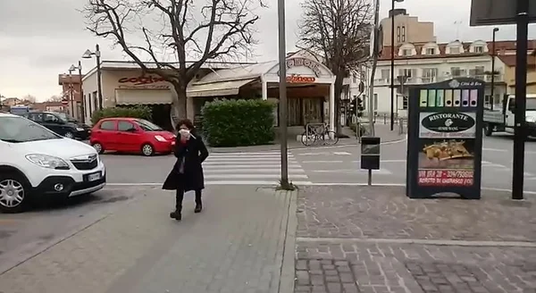 Mulher anda sozinha, com máscara, na rua em cidade italiana