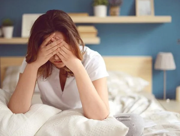 Mulher com as mãos no rosto deitada em uma cama de lençóis brancos