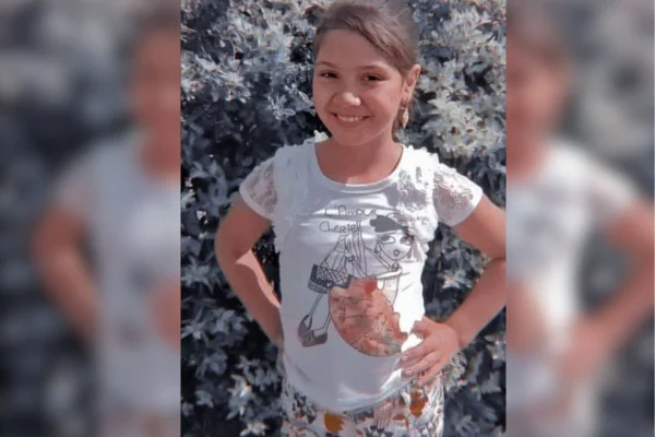imagem colorida mostra criança com mãos na cintura. menina usa blusa branca com desenho, tem cabelo liso e castanho, e sorri para a foto - metrópoles
