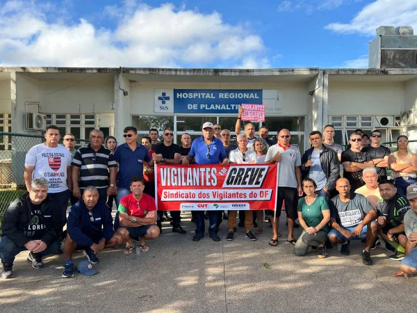 Imagem de multidão de pessoas em frente a prédio com cartazes vermelhos anunciando greve. Na placa do prédio: HRP