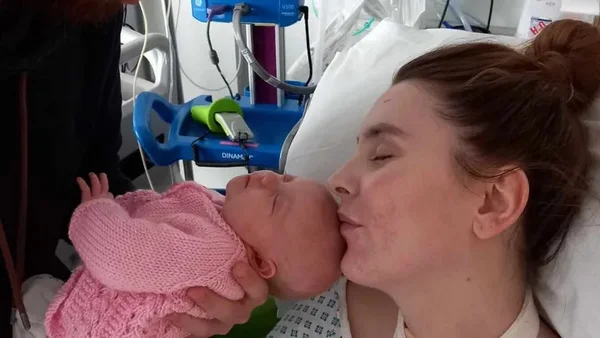Foto mostra Becky Prout em uma cama de hospital dando um beijo em seu bebê recém-nascido após tratamento para a doença do cérebro em chamas