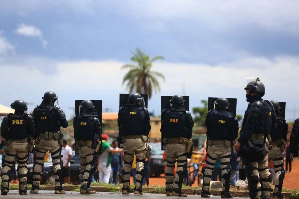 Policiais rodoviários federais formam barreira com escudos e fortemente equipados para desocurpar bloqueio em rodovia por apoiadores bolsonaristas. Eles são vistos de costas na cidade goiana de Luziânia - Metrópoles