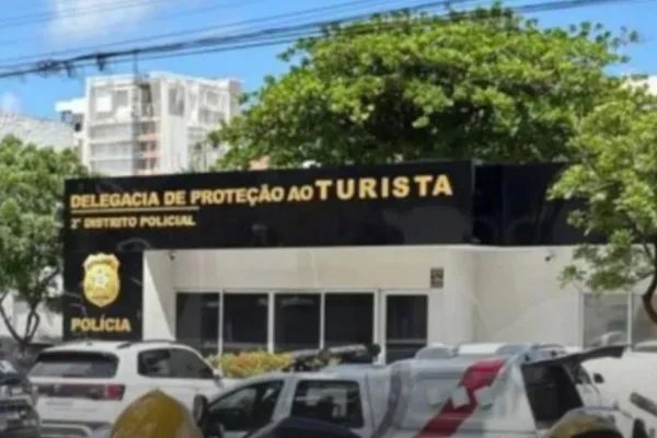 Imagens coloridas mostram frente de delegacia de polícia, paredes claras e faixa preta no alto com as inscrições 2ª Delegacia de Proteção ao Turista, viaturas estacionadas na frente do DP