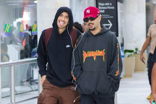 Pedro Sampaio e Henrique Meinke dividindo fone de ouvido no aeroporto - Metrópoles